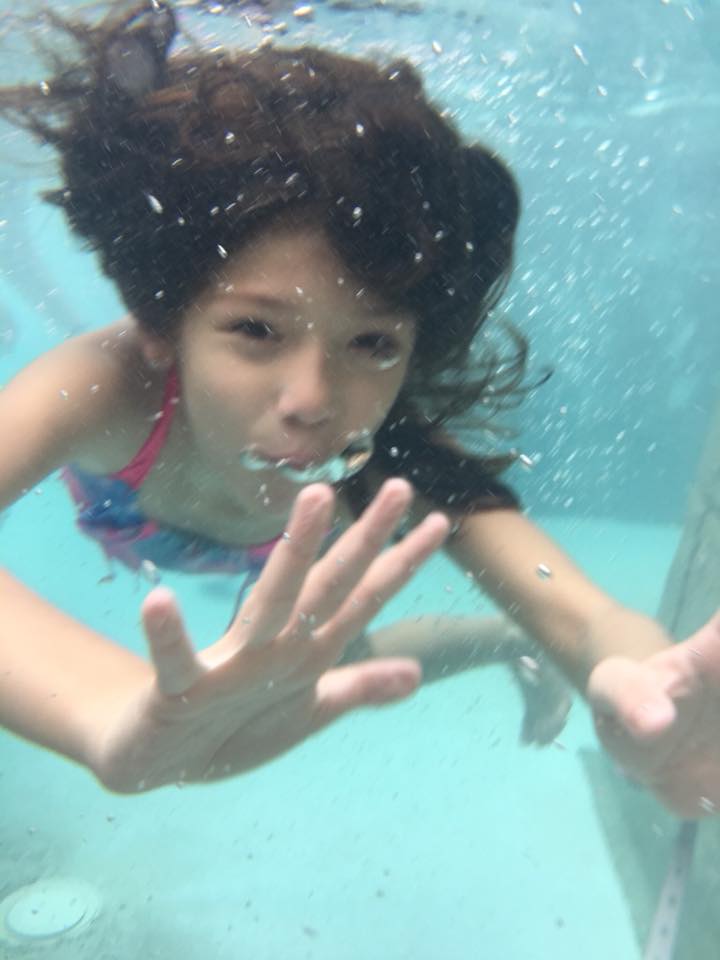 A little girl is swimming underwater in a pool.