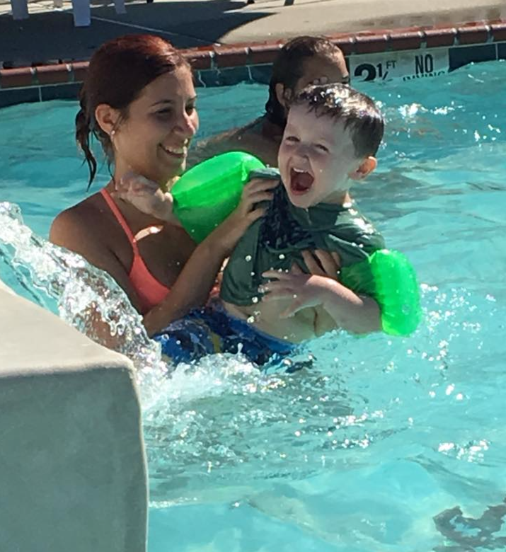 A woman is holding a child in a pool with a no diving sign in the background