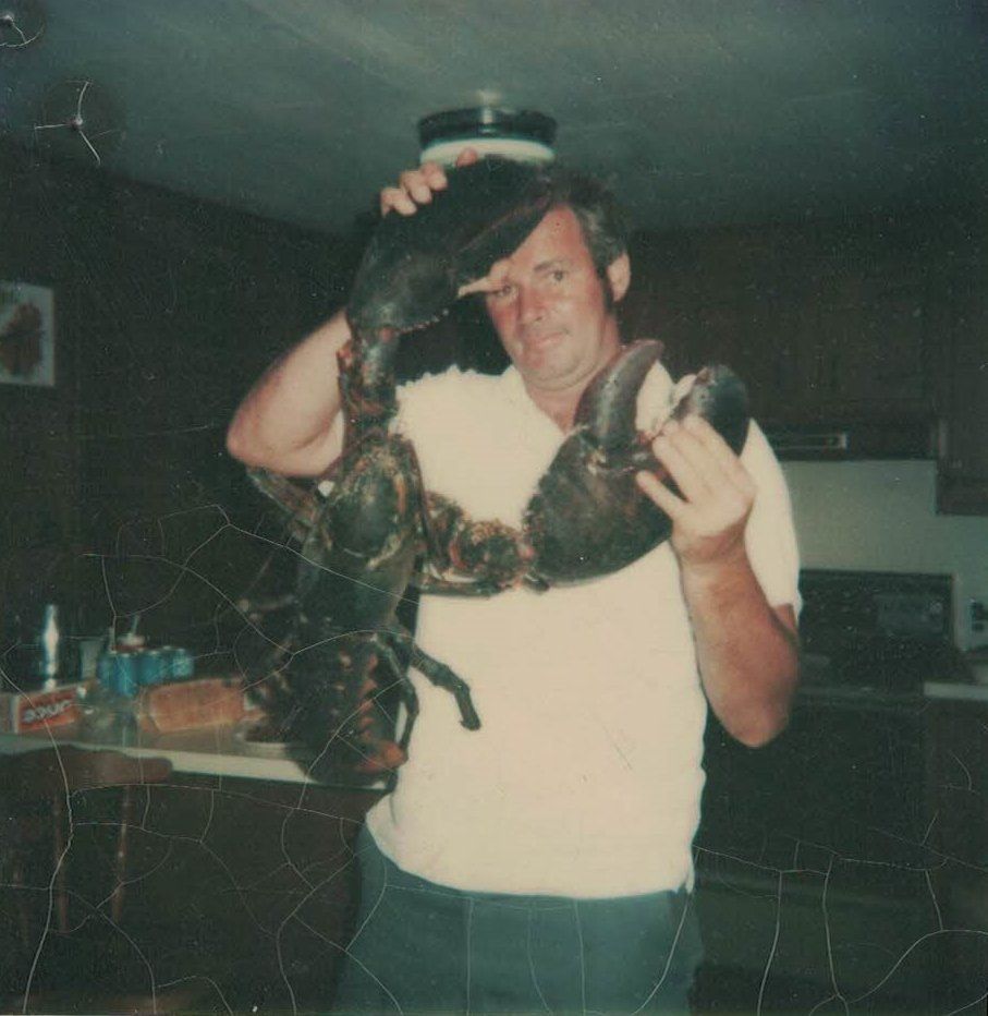 A man in a white shirt is holding a large lobster on his head