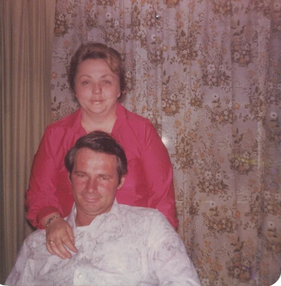 A man and woman are posing for a picture in front of a floral curtain.