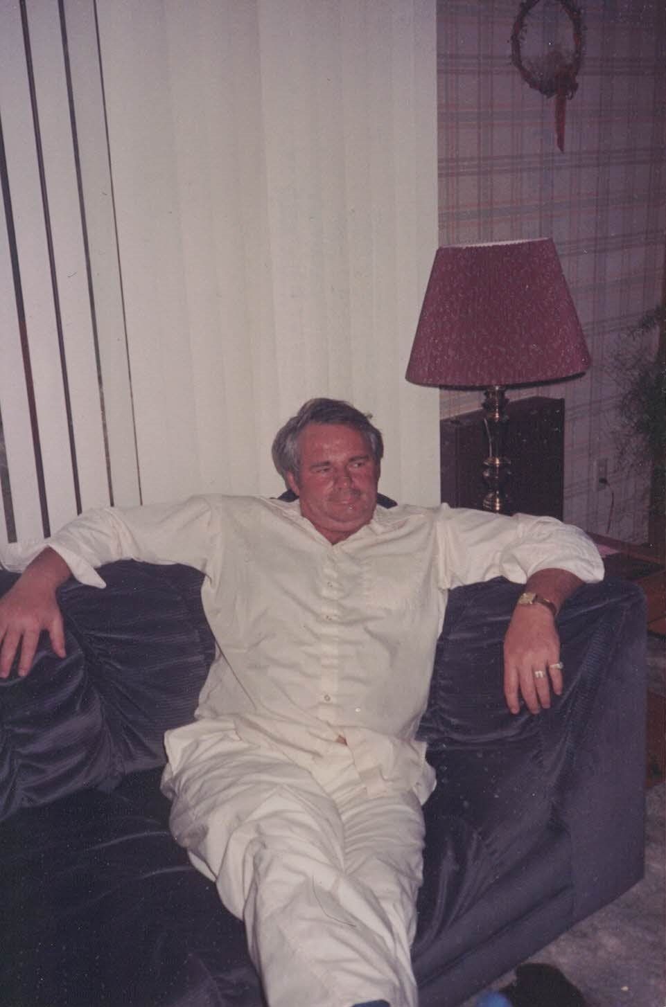 A man in a white shirt is sitting on a black couch with his arms crossed.