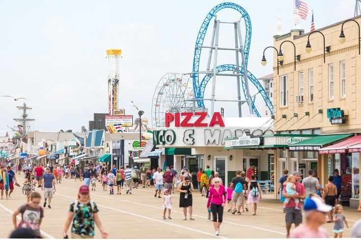 A crowd of people are walking down a boardwalk in front of a roller coaster.