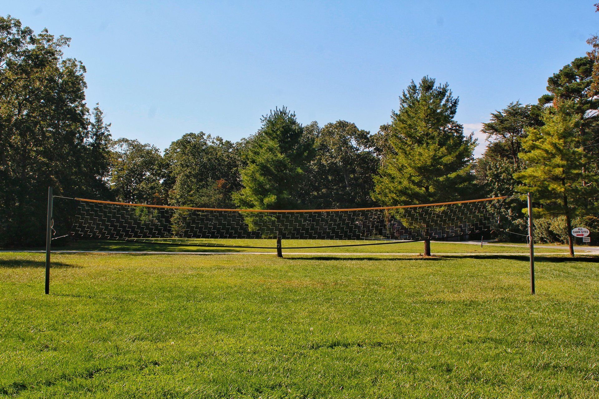 A volleyball net is in the middle of a grassy field surrounded by trees.