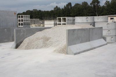Blocchi di cemento e ghiaia in un piazzale industriale all'aperto con alberi sullo sfondo.