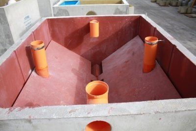Serbatoio d'acqua in cemento con pareti inclinate rosse e tubi arancioni all'interno.