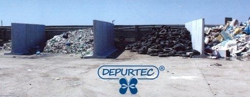 Area di riciclaggio dei rifiuti Depurtec con cumuli di materiali selezionati dietro cassonetti metallici.