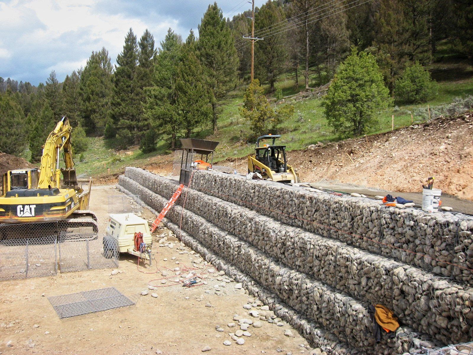 A cat excavator is working on a rock wall.