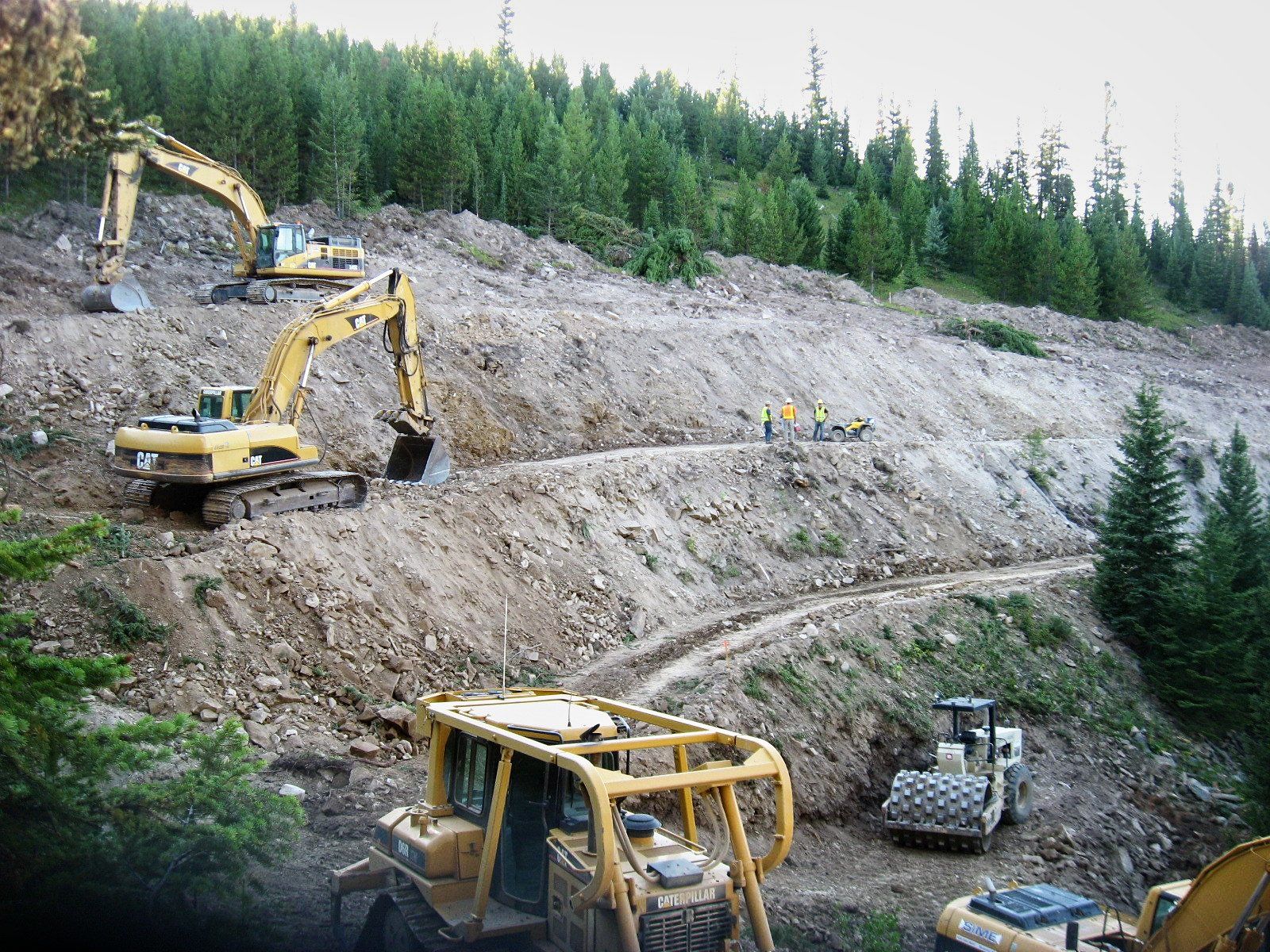 A group of construction vehicles are working on a hillside.