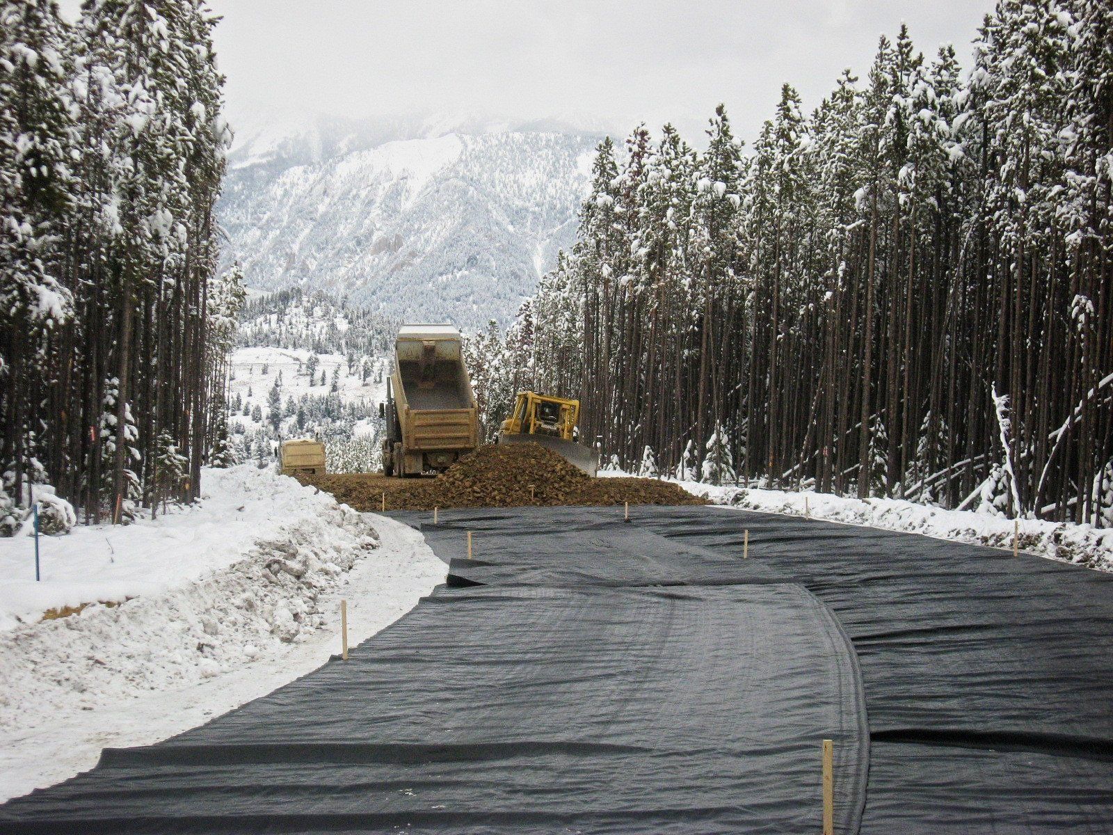 A dump truck is dumping dirt on a snowy road.