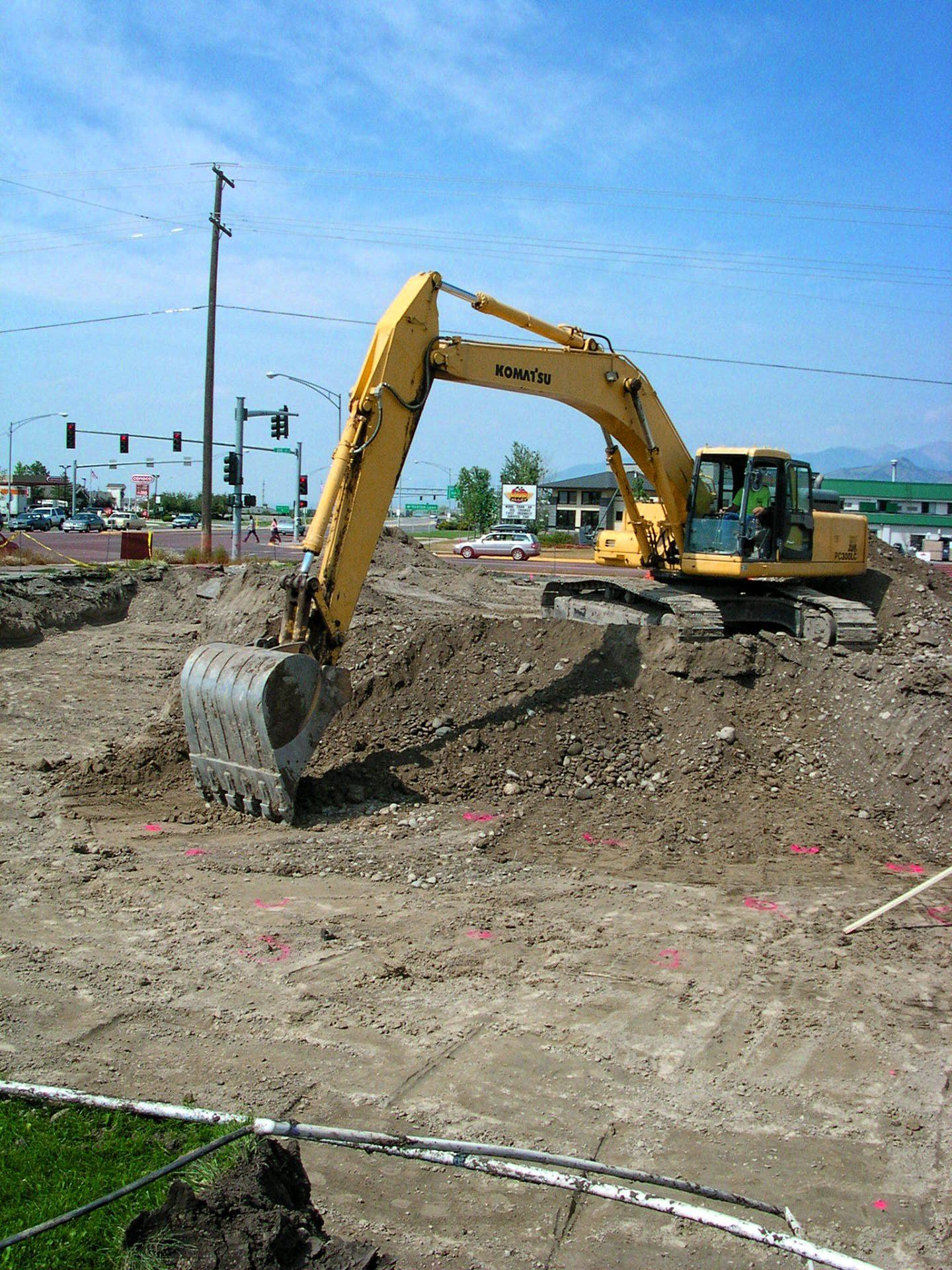 A yellow excavator is digging a hole in a dirt field