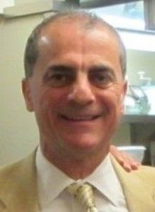 Man in a beige suit smiling, looking at the camera.