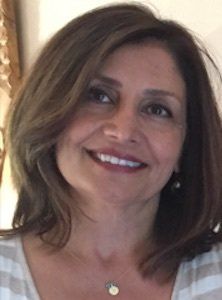 Woman with brown hair, smiling, looking upward. Wearing a light-colored striped shirt.