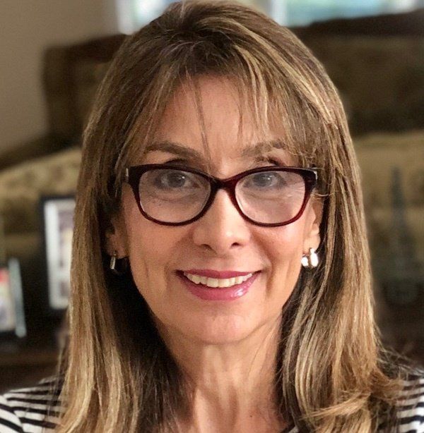 Woman with brown hair and glasses smiling. Wearing small earrings and a striped shirt.