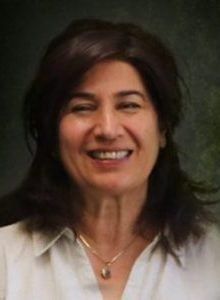 Woman with dark hair smiles, wearing a gold necklace and a button-down shirt.