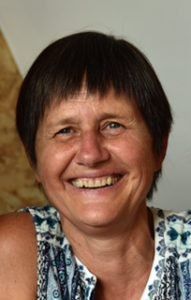 Woman with short dark hair smiles broadly, wearing a patterned sleeveless shirt.