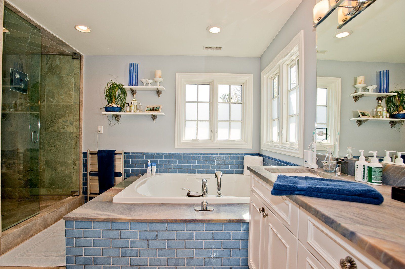 A bathroom with blue tiles , a tub , a sink and a mirror.