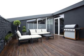 Outside Living Enclosure — Wooden Floor of Terrace with Plants and Black Brick Wall in Clayton, NC