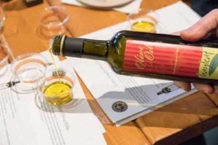 a person is pouring olive oil into a glass on a table .