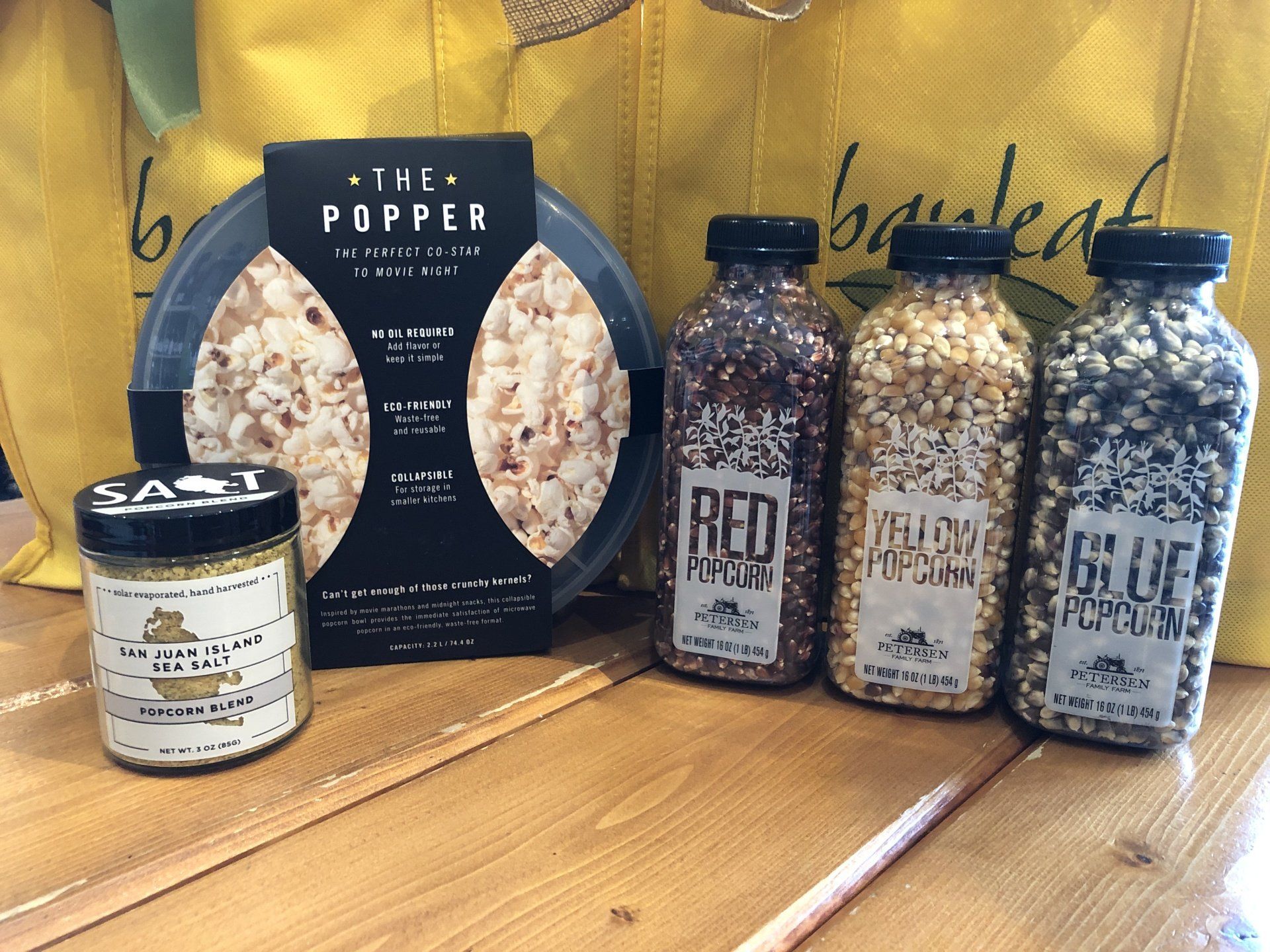 four bottles of popcorn are sitting on a wooden table next to a bag .