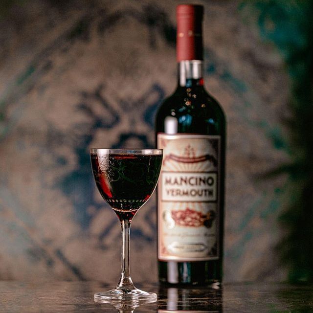 a bottle of mancino vermouth next to a glass of wine