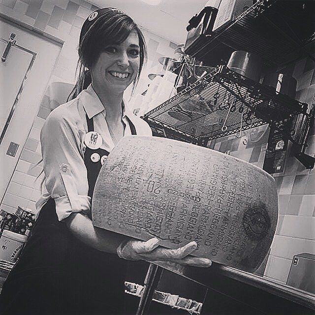 a woman in an apron is holding a large piece of cheese
