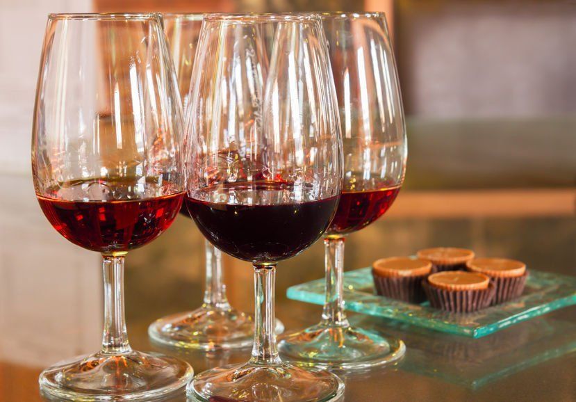 three glasses of red wine are sitting on a table next to a plate of chocolate cupcakes .