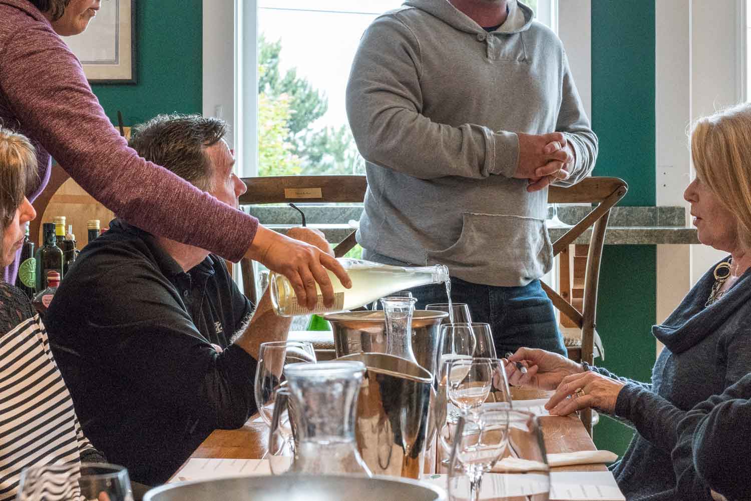 a group of people are sitting at a table while a man pours wine into a glass .