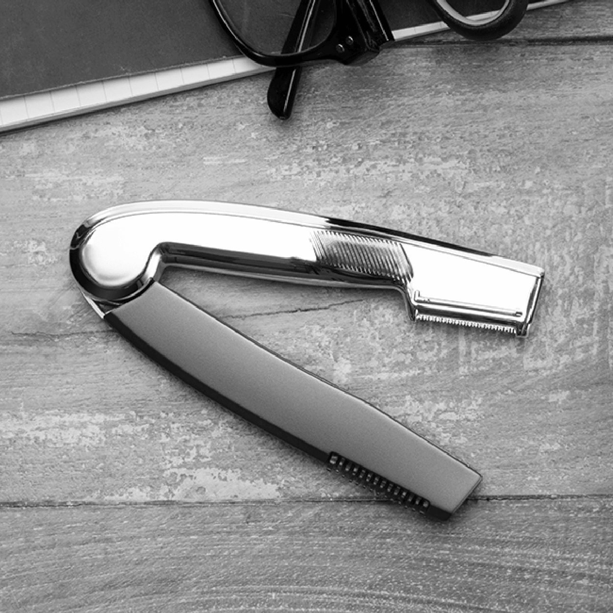 Chrome straight razor on a wood surface, with glasses in the background.