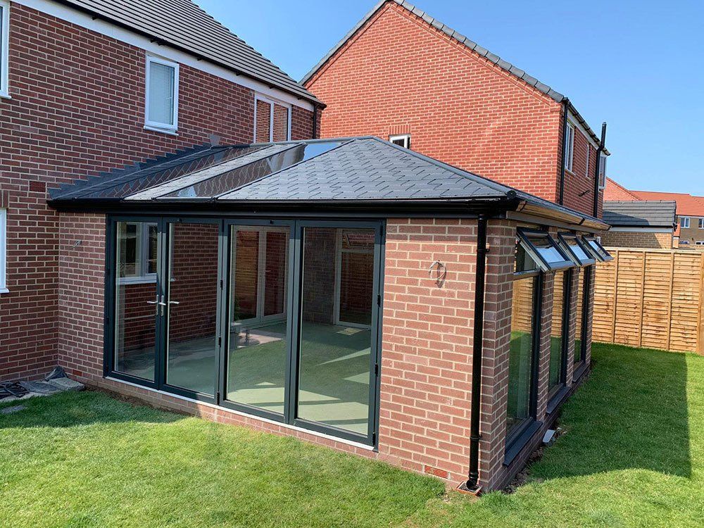 UPVC conservatory added to a new build property, Anthracite Grey grained effect frames with bi-fold door and Ultraframe 380 roof with glass panels – Ormesby St. Margaret, Great Yarmouth, Norfolk