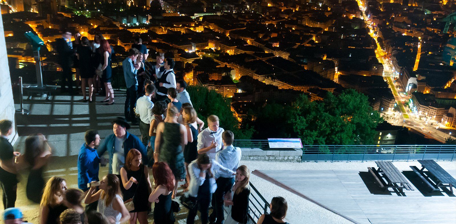 Un groupe de personnes se tient sur un balcon surplombant une ville la nuit.
