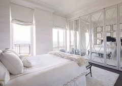 A bedroom with a bed , mirrored wardrobes , and lots of windows.