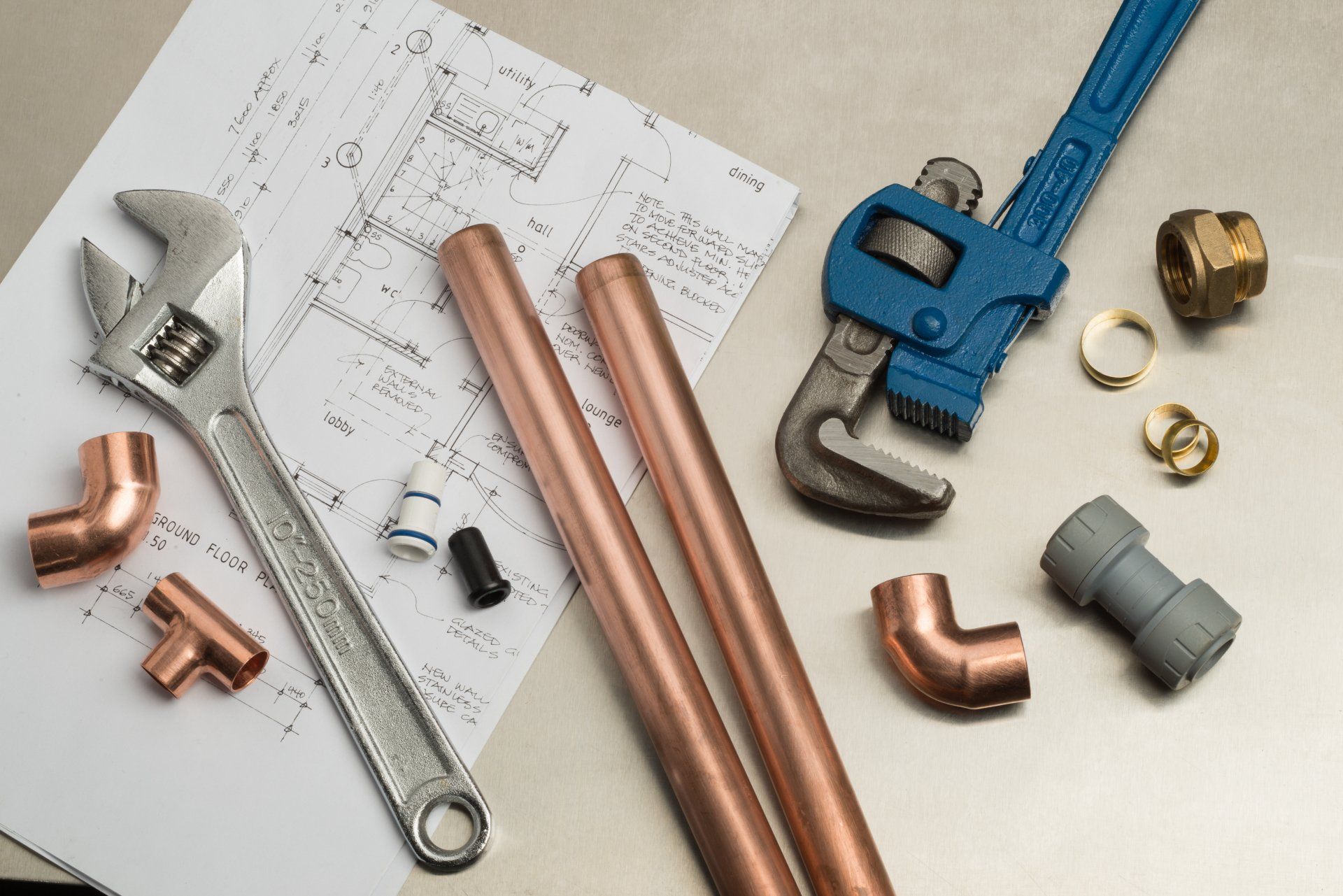 Assorted plumbing tools and copper pipes on a work surface, including a wrench and adjustable pipe cutter