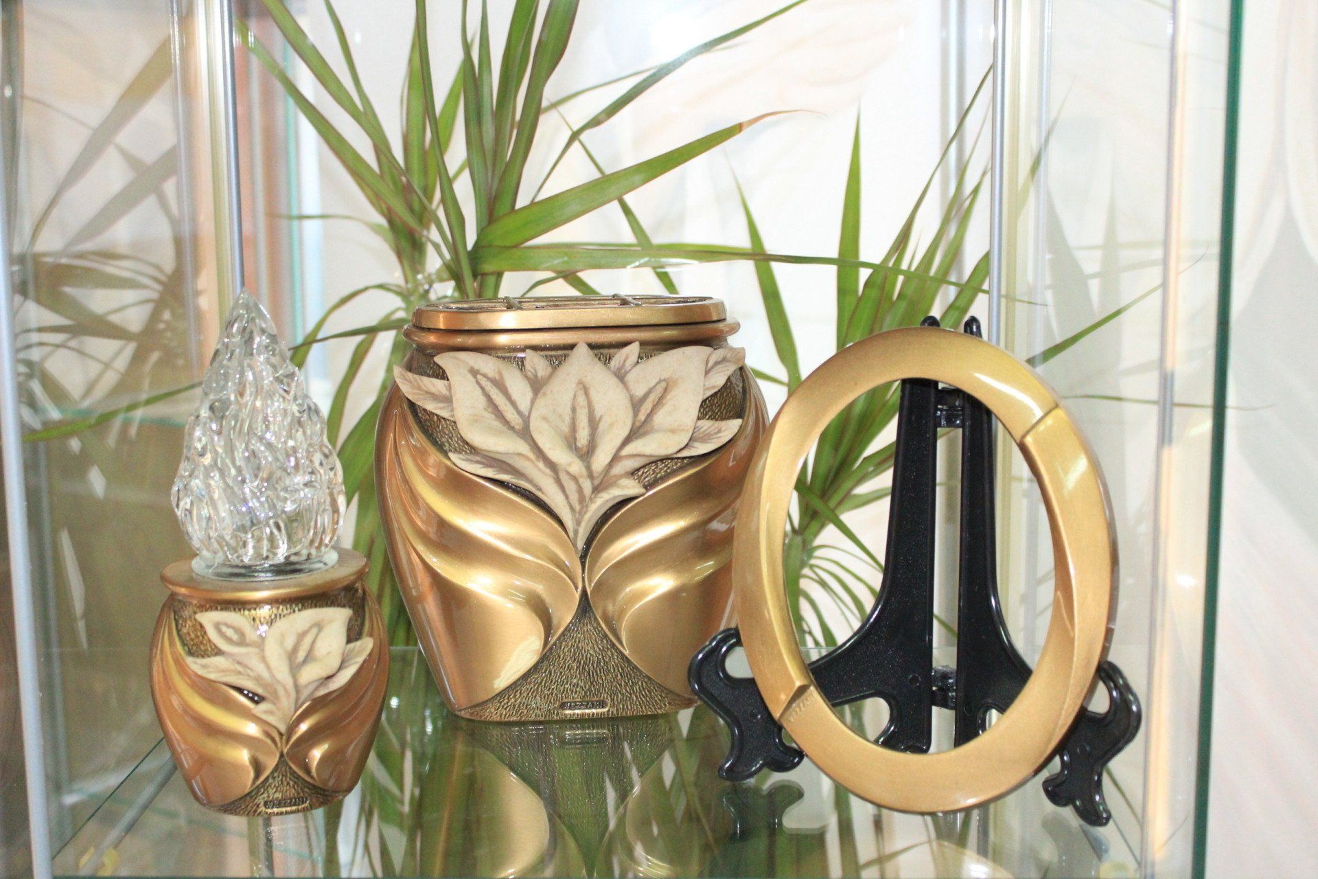 Vasi decorativi color oro e crema e cornice su una mensola di vetro con verde sullo sfondo.