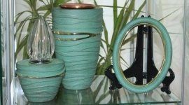 Vasi in ceramica color verde acqua con finiture dorate, una lampada di cristallo e una cornice ovale vuota color verde acqua su un supporto nero.