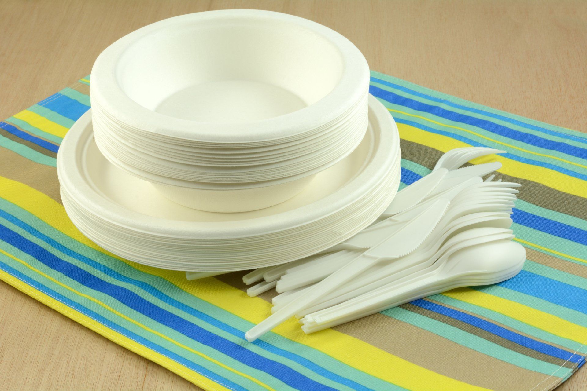 Una pila de platos, tazones, tenedores y cucharas de papel sobre una servilleta rayada.