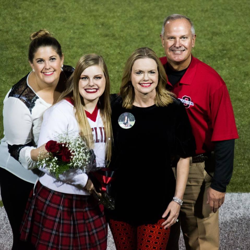 Family posing on a football field. A young woman holds flowers, flanked by her family, all smiling.
