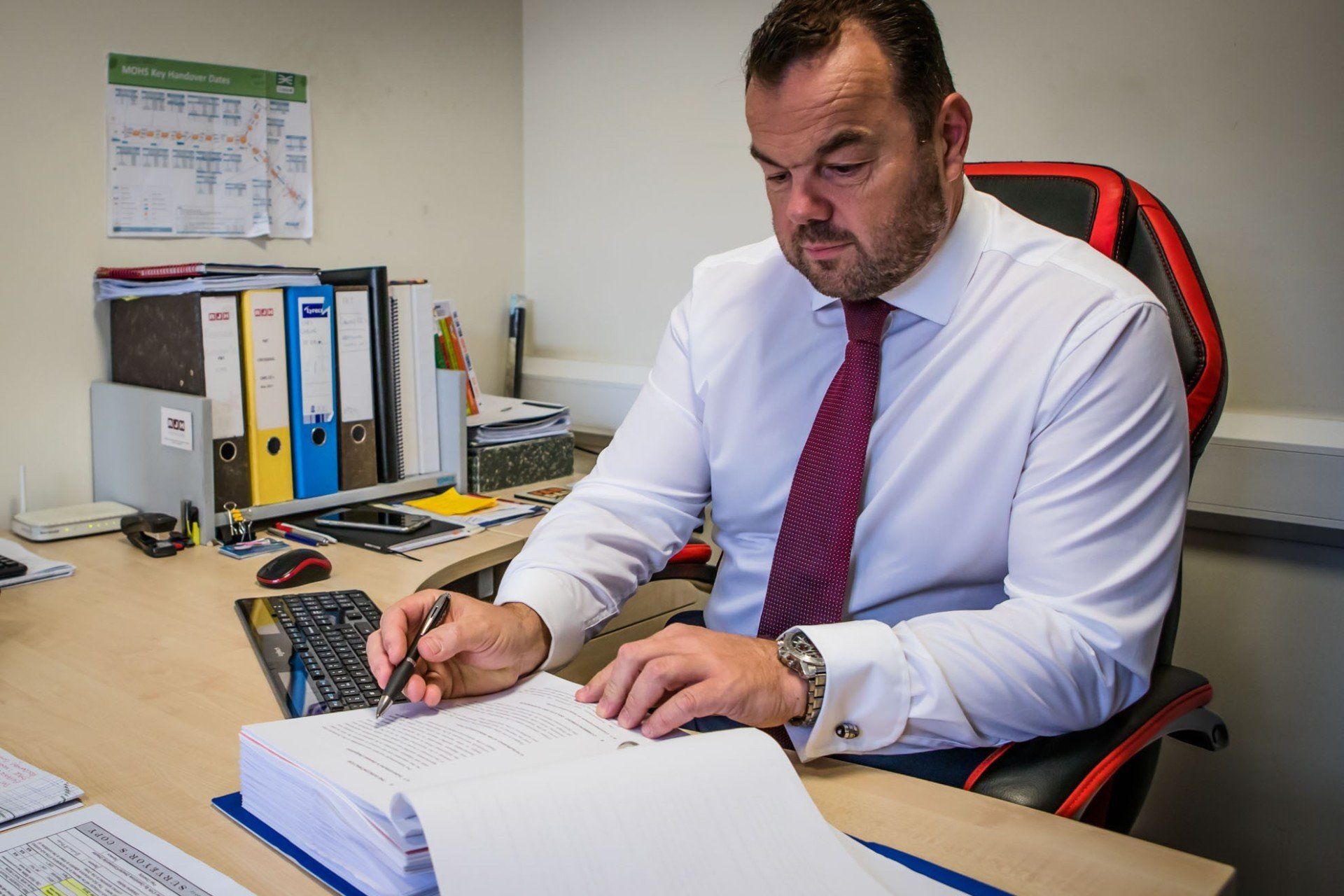 A man in a white shirt and red tie is sitting at a desk.