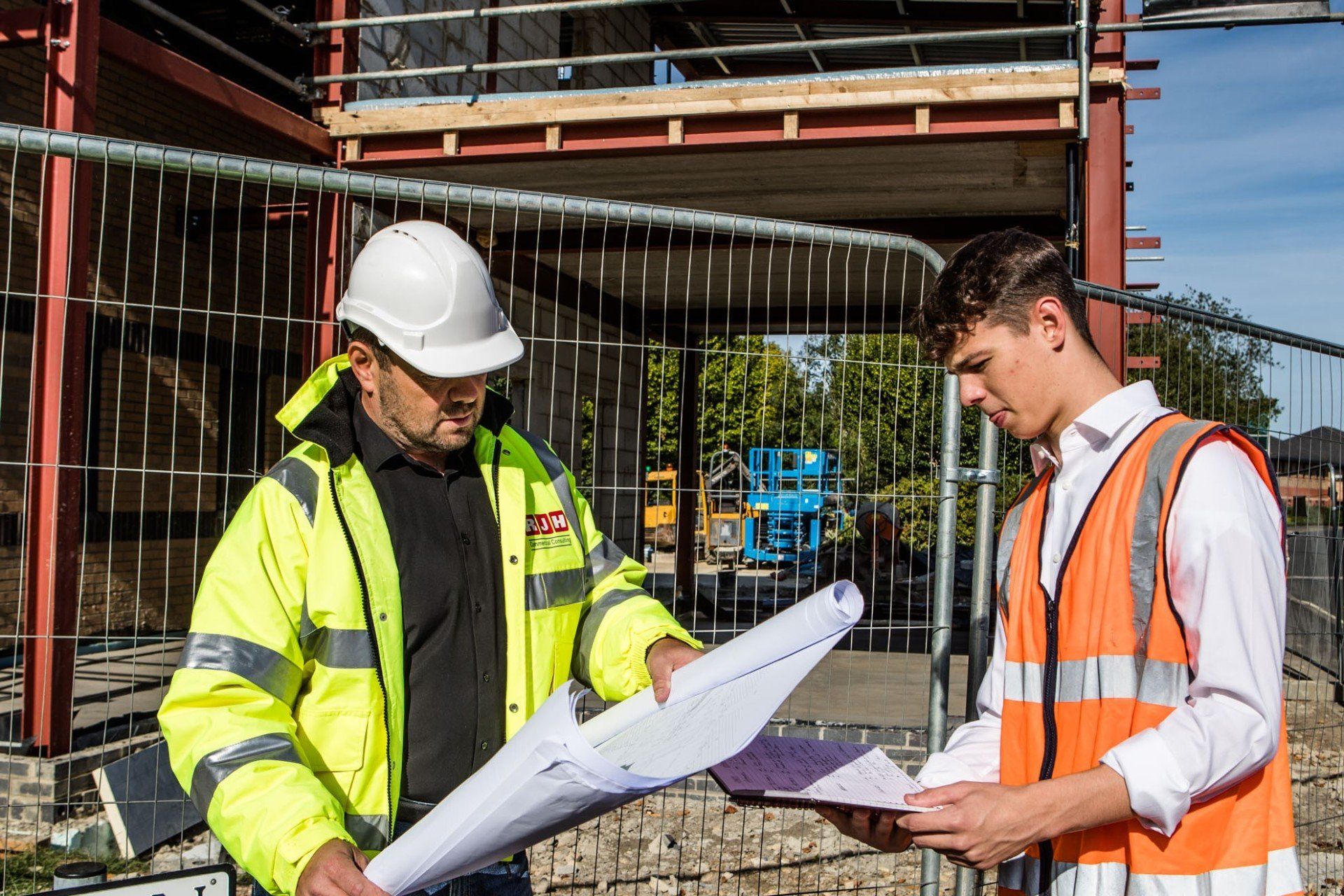 Two construction workers are looking at blueprints on a construction site.