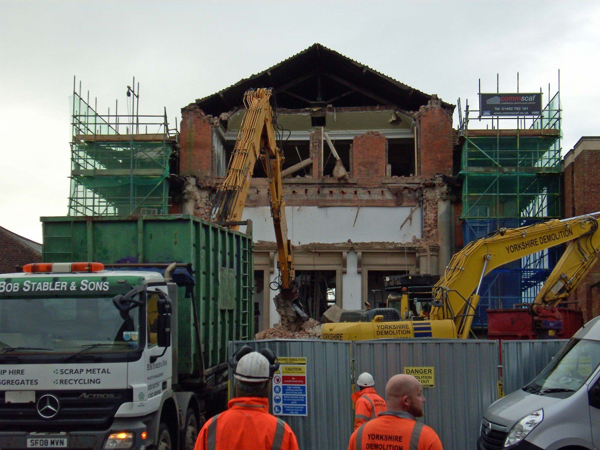 Construction workers are standing in front of a building that is being demolished