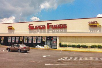Exterior of Super Foods grocery store with a car in front. Red sign, cream building.
