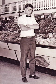 Man in uniform with crossed arms in front of produce displays.