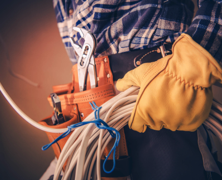 électricien avec ceinture à outils et pinces tenant une bobine de fils