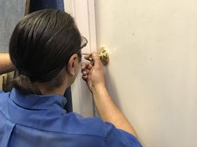 A woman in a blue shirt is locking a door with a screwdriver.
