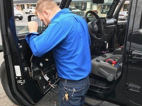A man in a blue shirt is working on the inside of a black jeep.