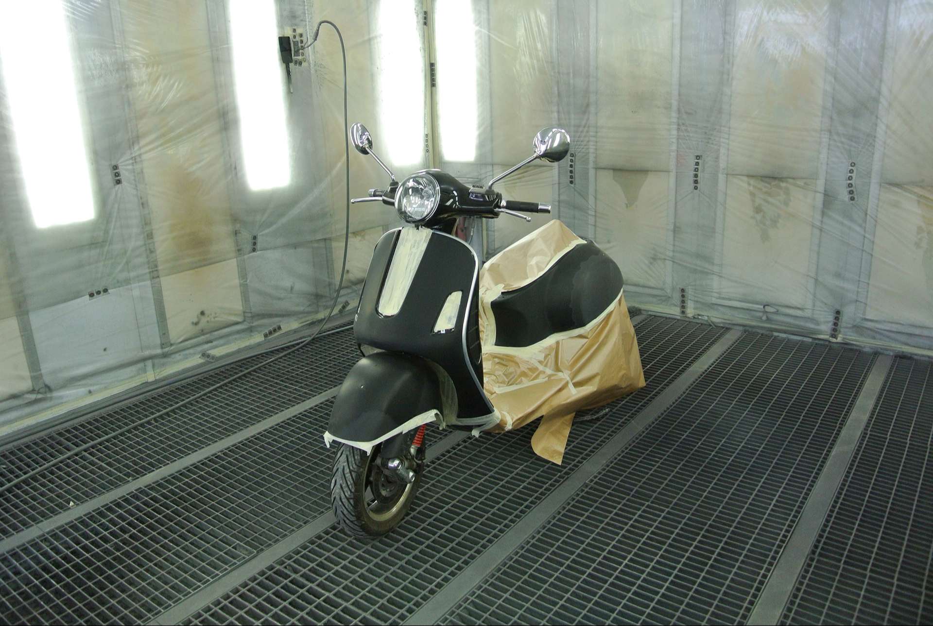 Scooter Vespa noir dans une cabine gyclage