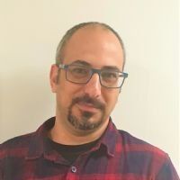 גבר עם משקפיים וזקן תיש, לובש חולצה משובצת אדומה, מחייך למצלמה.