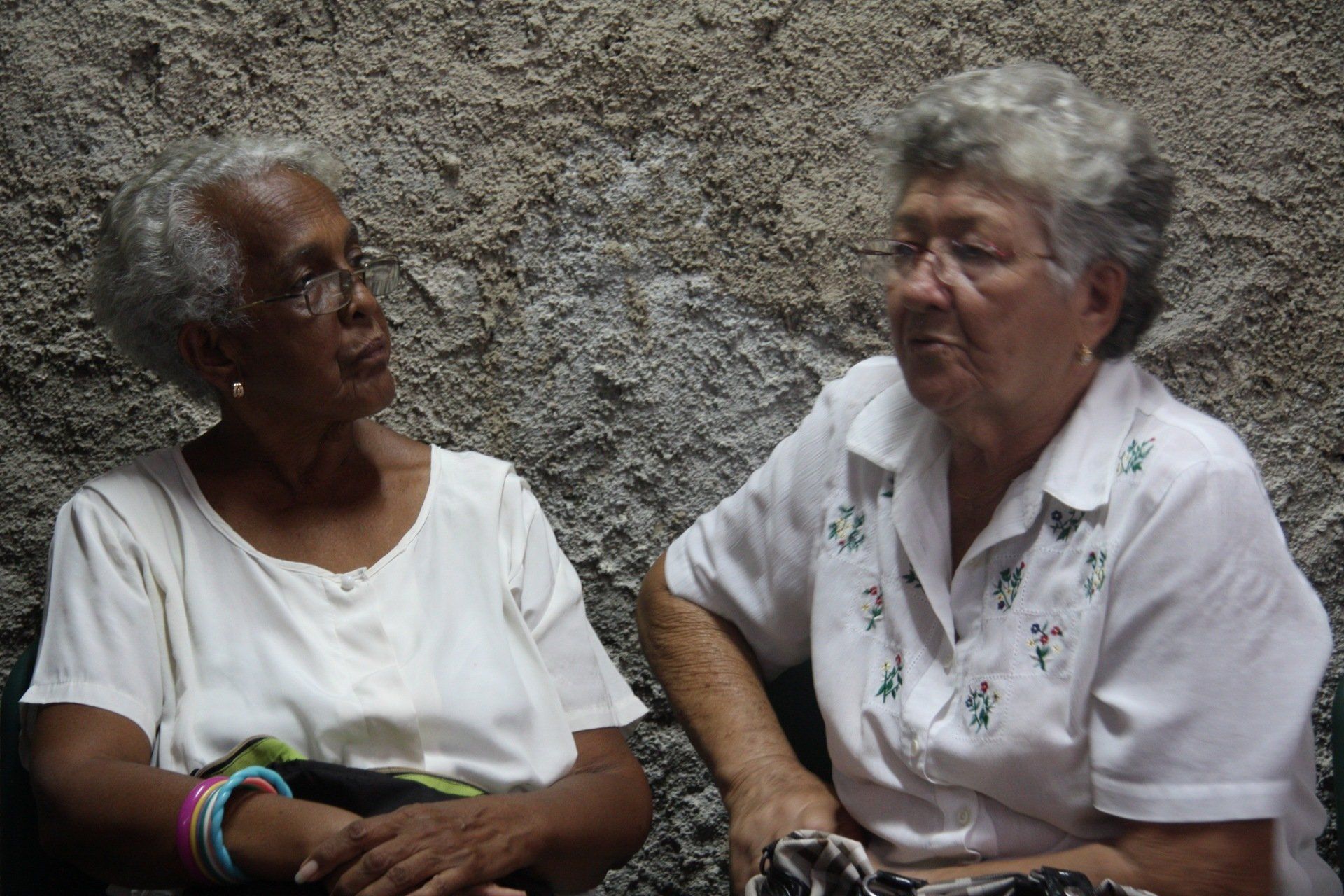 Two women seated against a rough wall, talking and facing each other.