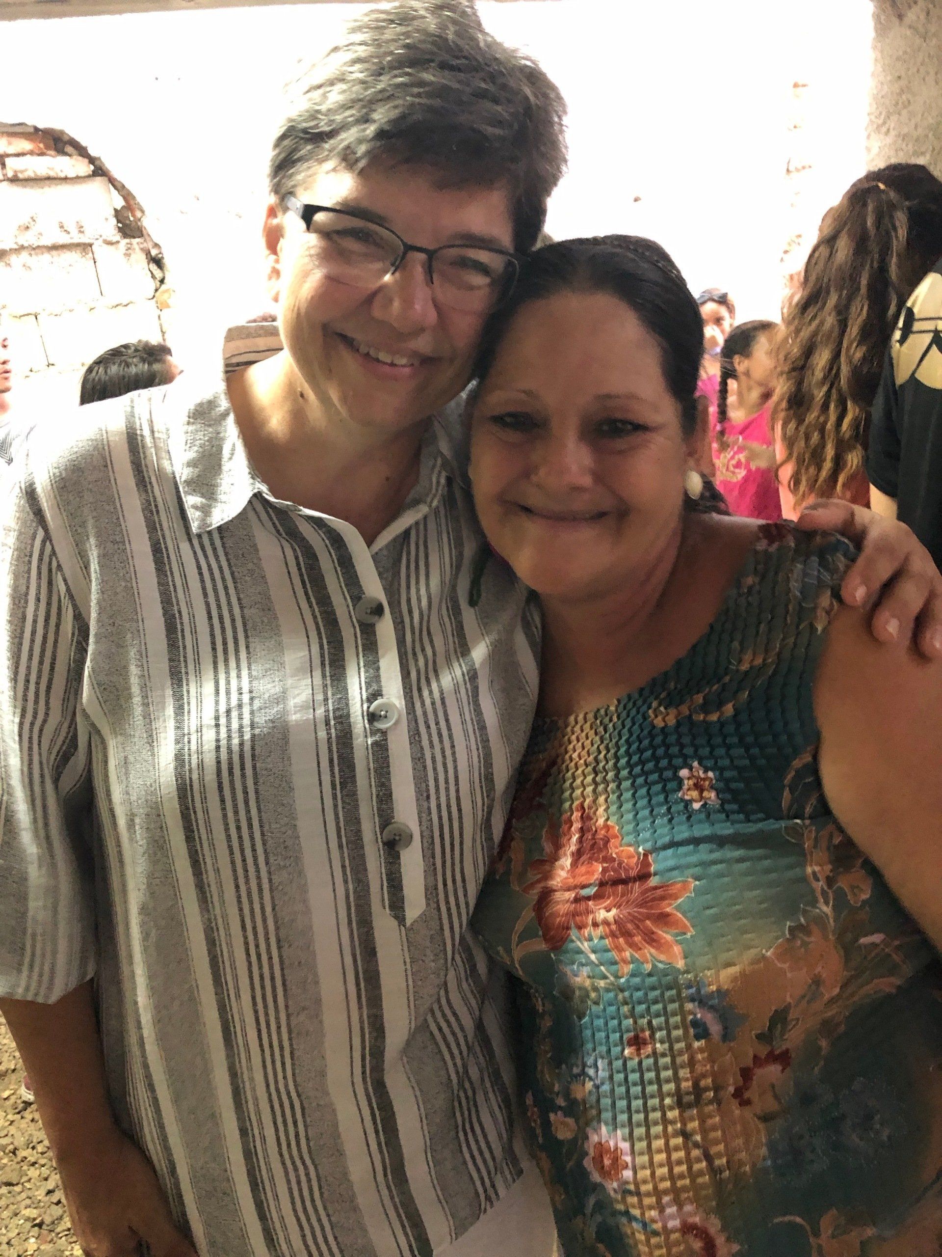 Two people smiling and posing together indoors, one in a striped shirt and one in a floral top.