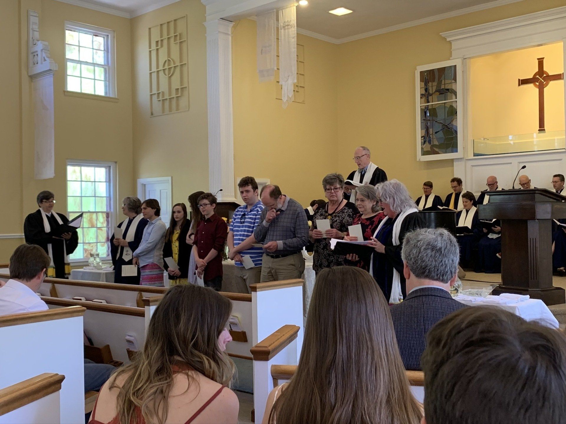Congregation standing in church sanctuary during service, with cross and pastor at the front.
