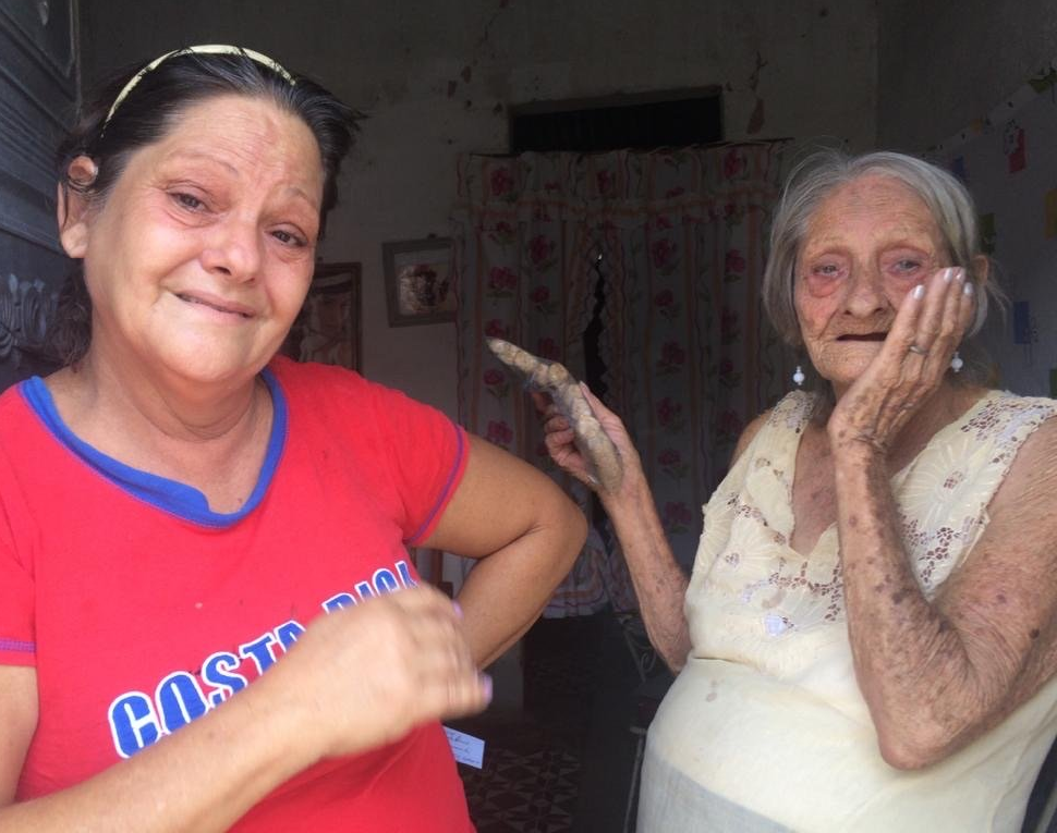 Two women smiling in a doorway, one in a red shirt and one in a white shirt with flour on her hands.